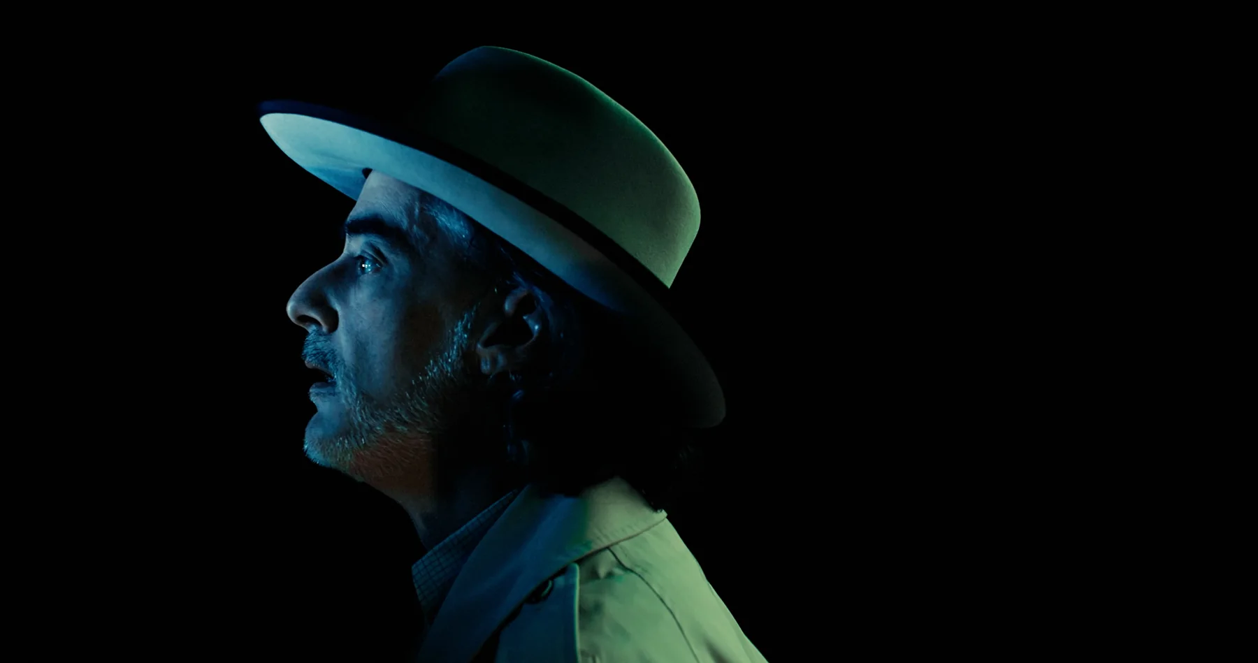 P.T. Mitchell in his hat, illuminated by a cold cyan light.